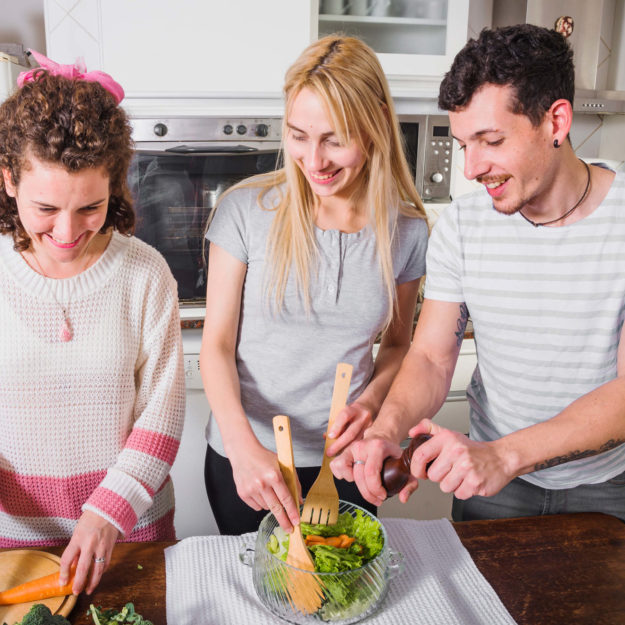 Zwei Frauen und ein Mann bereiten gemeinsam einen Salat zu.